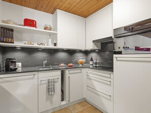 Une cuisine moderne avec des meubles blancs, un plan de travail noir et un plafond en bois.