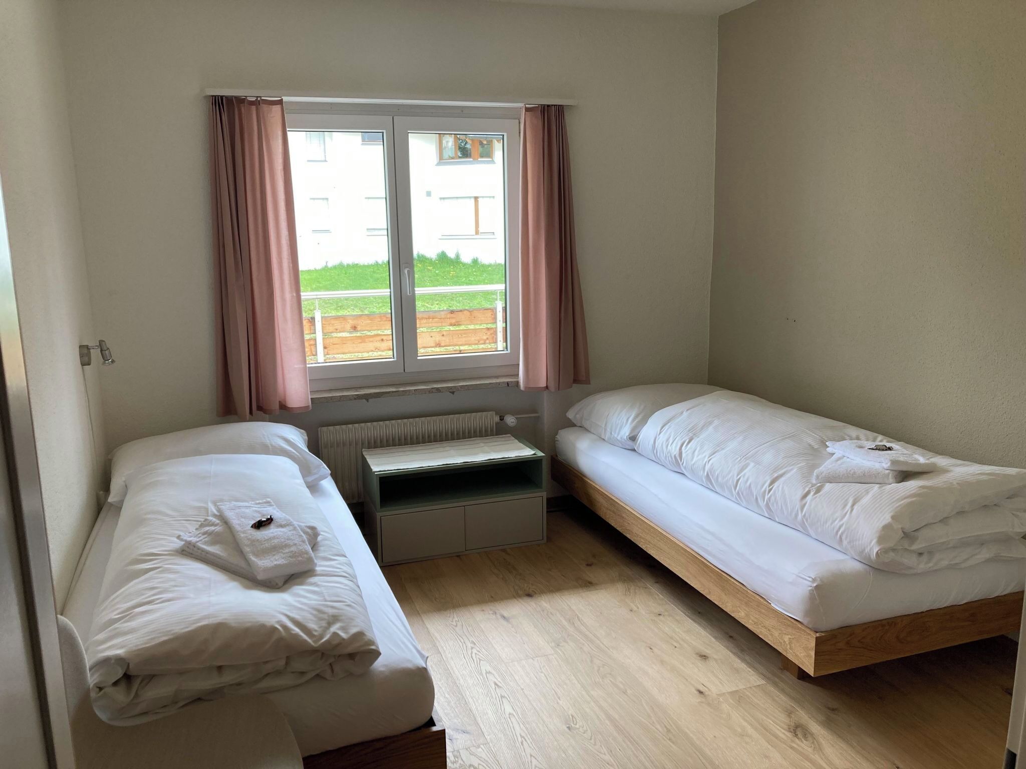Ein kleines, sauberes Zimmer mit zwei Einzelbetten, einem Fenster mit Vorhängen und einer Heizung.