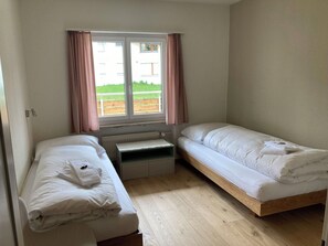 Una habitación pequeña y limpia con dos camas individuales, una ventana con cortinas y un radiador.