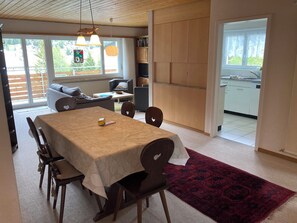 A dining area with a table, chairs, and a red rug. There is a kitchen visible through an open door. - Haus Montana 1/6 Appartement/Fewo,   5-Bettwohnung by Interhome (Lenzerheide)
