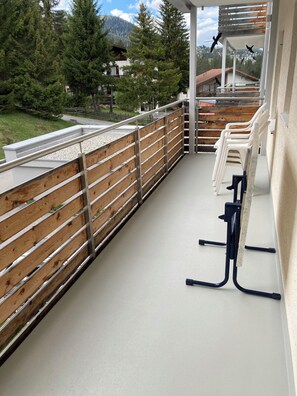 Ein Balkon mit Holzgeländer, einem weißen Boden und einer Reihe weißer Plastikstühle.