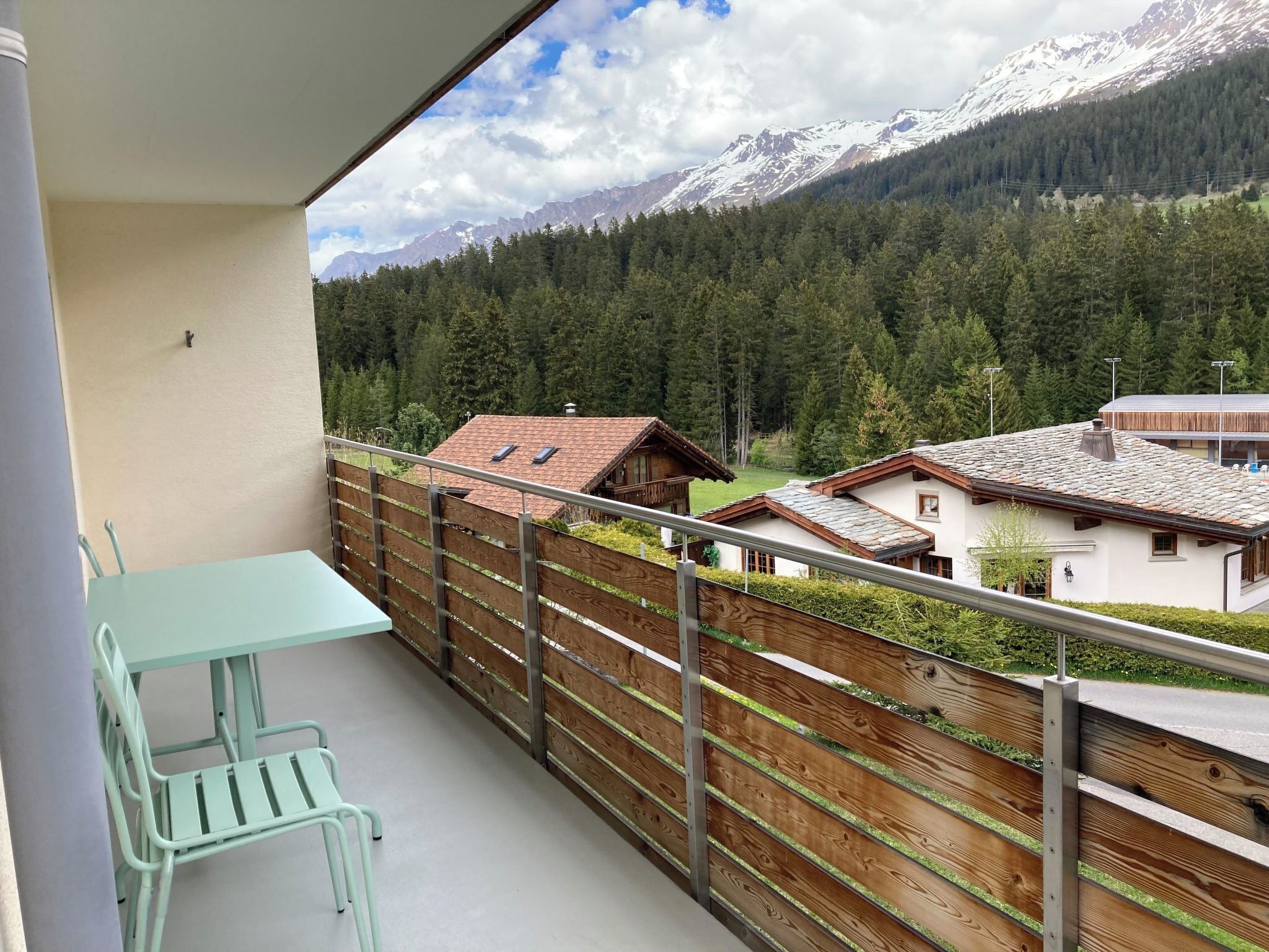 A balcony with a table and chairs, overlooking a mountainous landscape with houses and a wooden fence.