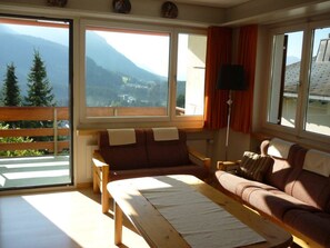 A room with a sofa, a table, and a view of mountains through large windows. - Haus Curver Bächtold Appartement/Fewo,   5-Bettwohnung (4.5 Zimmerwohnung) by Interhome (Valbella)