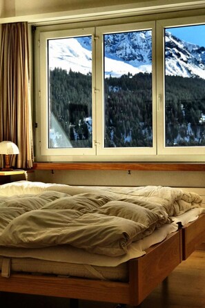 A bed with a view of a snowy mountain landscape through a window. - Haus Curver Bächtold Appartement/Fewo,   5-Bettwohnung (4.5 Zimmerwohnung) by Interhome (Valbella)