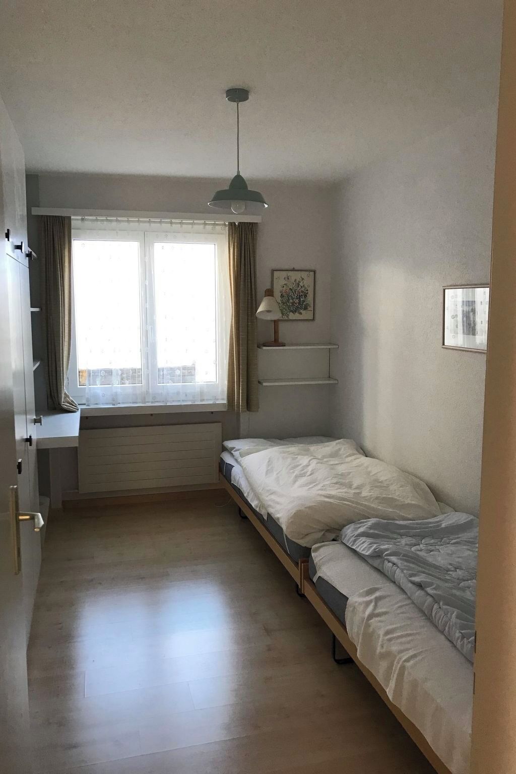 A small, single-bed room with a window, a desk, and a radiator.