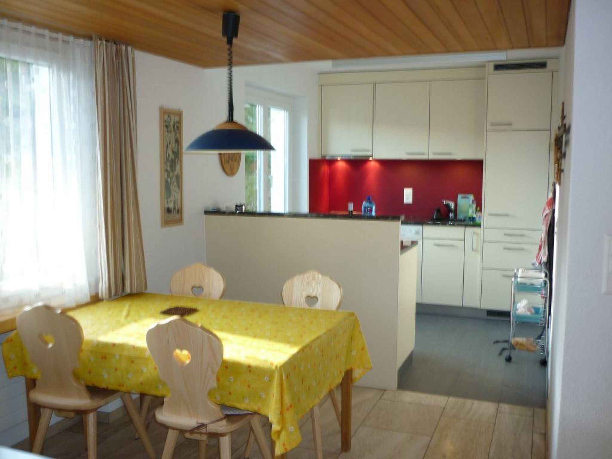 A dining area with a table and chairs, a kitchen with cabinets, and a ceiling fan.