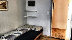 A small, single-bed room with a wooden floor, a wall-mounted shelf, and a door leading to another room. - Haus Curver Bächtold Appartement/Fewo,   5-Bettwohnung (4.5 Zimmerwohnung) by Interhome (Valbella)