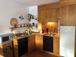 Eine kleine Küche mit Holzausstattung, einer Mikrowelle, einem Geschirrspüler, einem Herd und einem Kühlschrank.