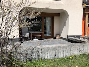 Un patio con mesa y sillas, un borde de hormigón y vistas a un edificio con terraza de madera.