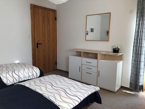 Ein Schlafzimmer mit zwei Betten, einem Holzschrank, einem Spiegel und einem kleinen Tisch mit einer Pflanze.