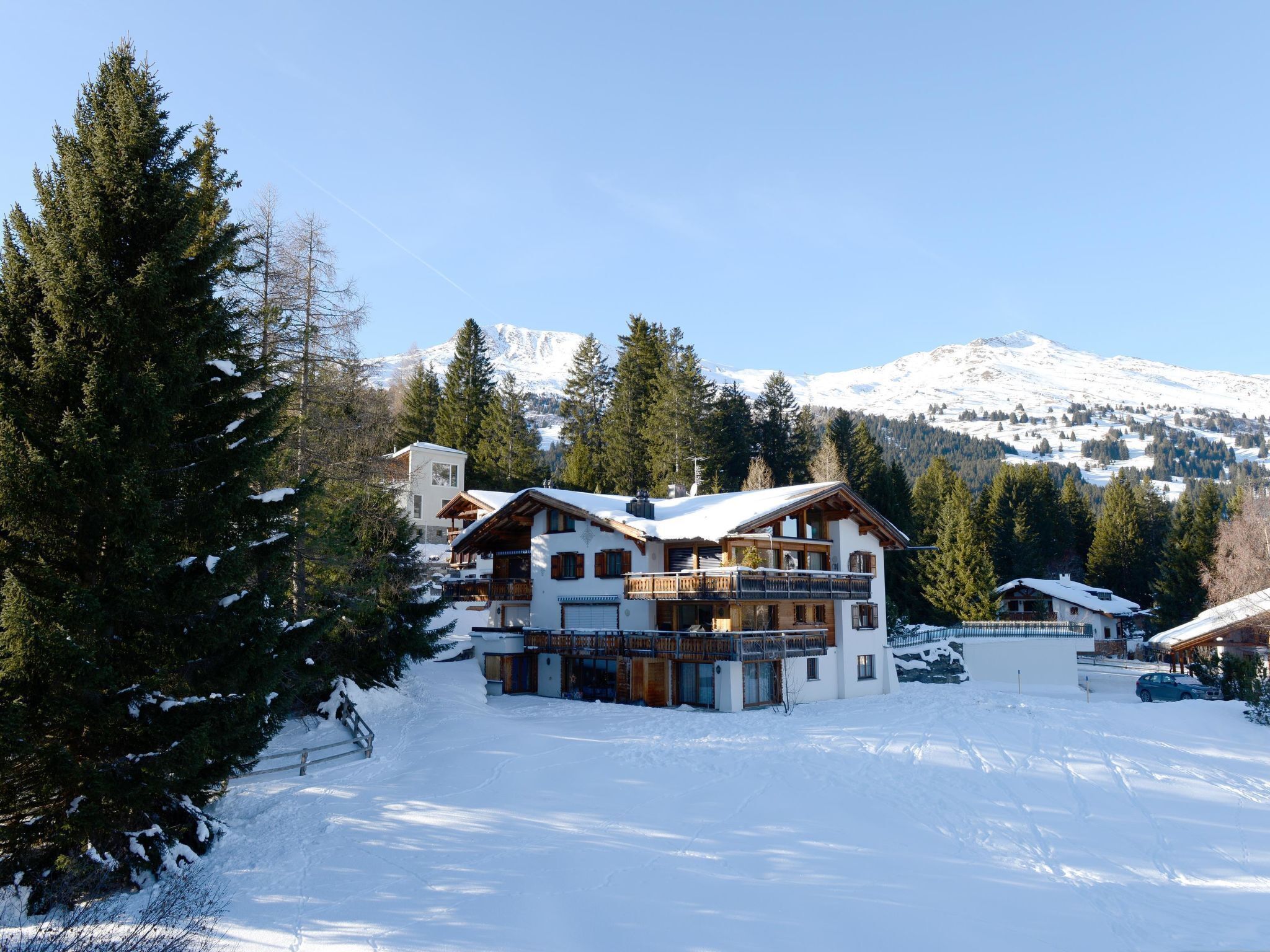 Een meerlaags chalet met een sneeuwbedekte dak, omringd door hoge dennen en een berg op de achtergrond.