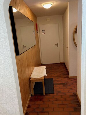 Ein schmaler Flur mit einer Holzbank, einem Spiegel und einer Tür mit einem Schild.