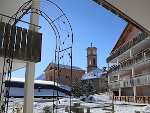 Ein verschneites Freigelände mit einem Glockenturm, einem Holzzaun und einem Gebäude mit Balkonen.