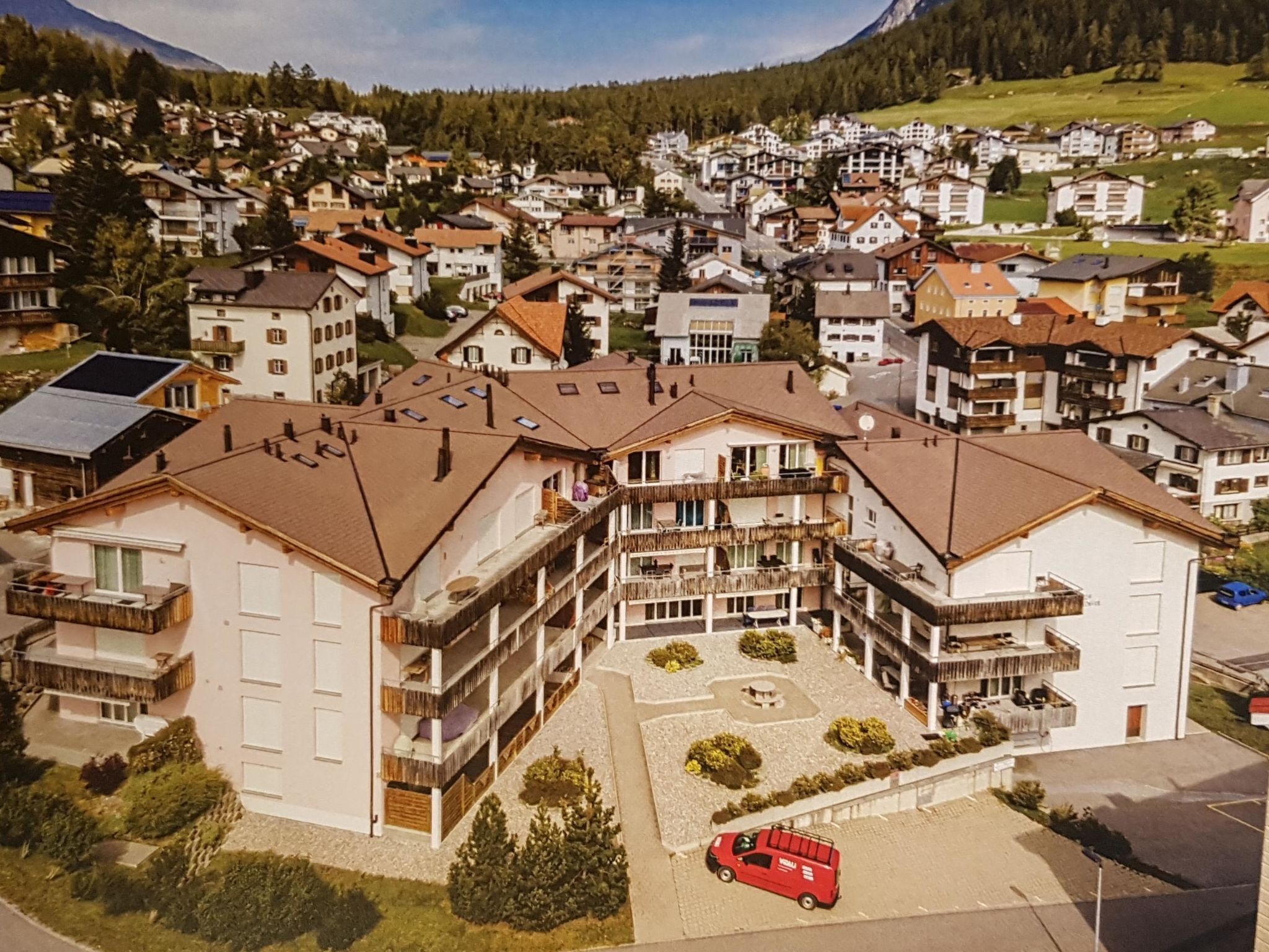 Ein mehrstöckiges Hotel mit Balkonen, einem Parkplatz und einem roten Auto davor.