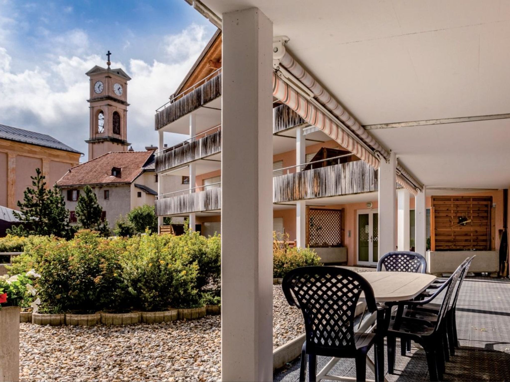 Une cour avec un espace repas, un bâtiment doté d’une tour horloge et un jardin.