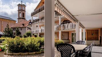 Une cour avec un espace repas, un bâtiment doté d’une tour horloge et un jardin.
