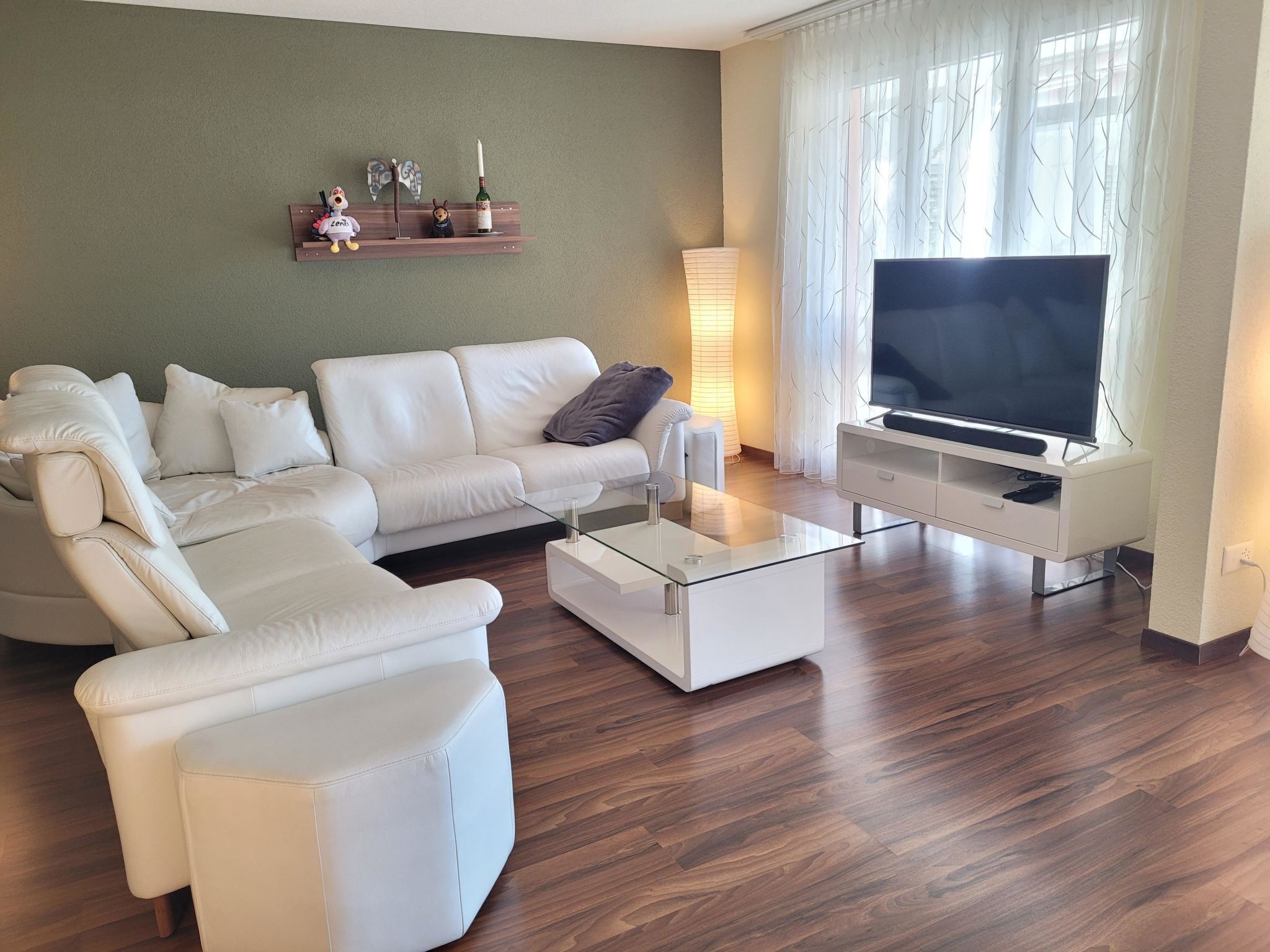 Ein modernes Wohnzimmer mit einem weißen Sofagarnitur, einem Glastisch, einem Flachbildfernseher und Holzboden.