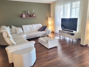 A modern living room with a white sofa set, a glass coffee table, a flat-screen TV, and a wooden floor. - Ferienwohnung zBERG Appartement/Fewo, Dusche und Bad, WC, 3 Schlafräume by Interhome (Lantsch)