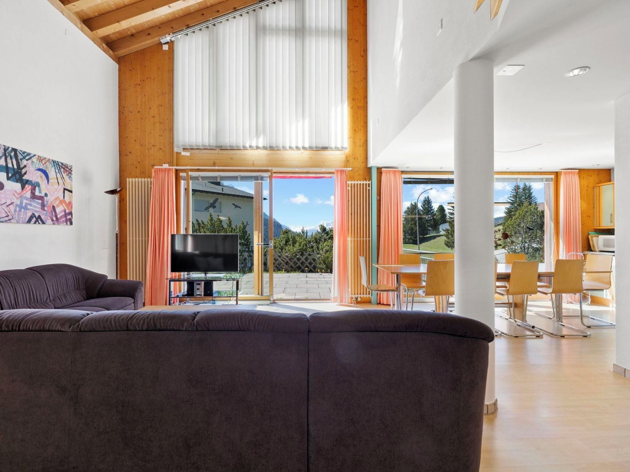 A modern living room with a large sofa, a flat-screen TV, and a dining area with chairs and a table.