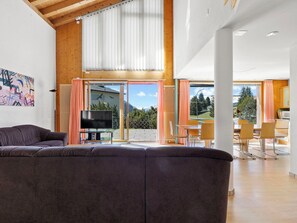 A modern living room with a large sofa, a flat-screen TV, and a dining area with chairs and a table. - Golden Peaks Ferienhaus Ferienhaus, Dusche und Bad, WC, 4 oder mehr Schlafräume by Interhome (Valbella)