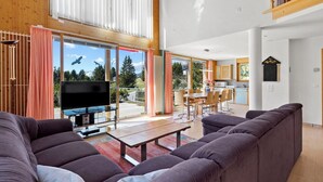 A spacious living room with a large flat-screen TV, a sofa, and a dining area with a table and chairs. - Golden Peaks Ferienhaus Ferienhaus, Dusche und Bad, WC, 4 oder mehr Schlafräume by Interhome (Valbella)