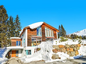 A two-story log cabin with a stone wall and snow-covered roof, surrounded by trees and mountains. - Golden Peaks Ferienhaus Ferienhaus, Dusche und Bad, WC, 4 oder mehr Schlafräume by Interhome (Valbella)