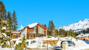 A wooden cabin with a snow-covered roof, surrounded by snow and trees, with a mountain in the background. - Golden Peaks Ferienhaus Ferienhaus, Dusche und Bad, WC, 4 oder mehr Schlafräume by Interhome (Valbella)