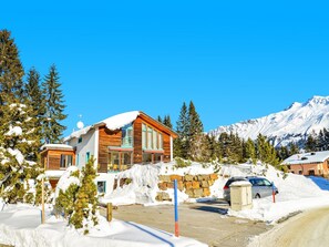 Eine Holzhütte mit schneebedecktem Dach, umgeben von Schnee und Bäumen, mit einem Berg im Hintergrund.