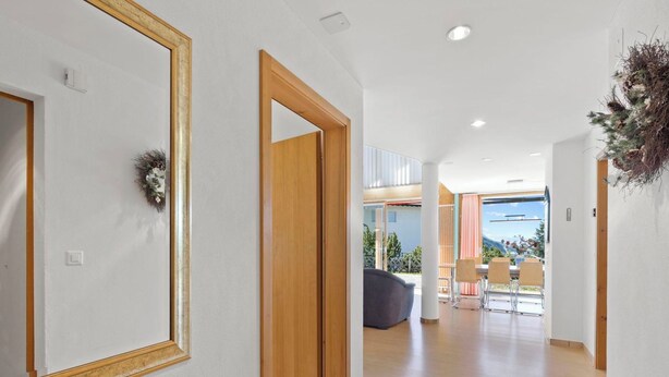 A hallway with a wooden door, a mirror, and a view into a living area with a sofa and chairs. - Golden Peaks Ferienhaus Ferienhaus, Dusche und Bad, WC, 4 oder mehr Schlafräume by Interhome (Valbella)