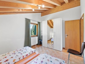 A bedroom with a bed, a chair, a wardrobe, and a window with curtains. - Golden Peaks Ferienhaus Ferienhaus, Dusche und Bad, WC, 4 oder mehr Schlafräume by Interhome (Valbella)