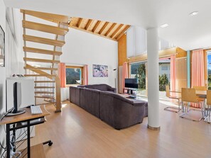 A modern living space with a wooden staircase, a grey sofa, a dining area with a table and chairs, and a computer setup. - Golden Peaks Ferienhaus Ferienhaus, Dusche und Bad, WC, 4 oder mehr Schlafräume by Interhome (Valbella)