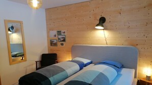 Makuuhuoneessa on sänky, tuoli, peili ja puinen seinä.