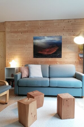 A living room with a blue sofa, wooden coffee table, and a painting on the wall. - CANOLS#32 Appartement/Fewo 4-Bettwohnung (2-Zimmerwohnung) by Interhome (Valbella)
