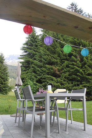 An outdoor patio with a table and chairs, surrounded by greenery and a mountain backdrop. - CANOLS#32 Appartement/Fewo 4-Bettwohnung (2-Zimmerwohnung) by Interhome (Valbella)