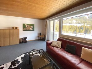 Una sala acogedora con un sofá de cuero rojo, una mesa de centro de vidrio con estampado de vaca, un aparador de madera y un cuadro de vaca en la pared.