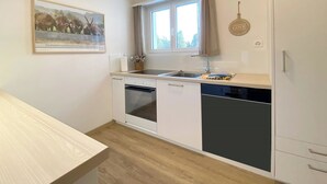 Een kleine keuken, voorzien van een vaatwasser, oven en een raam boven de spoelbak.