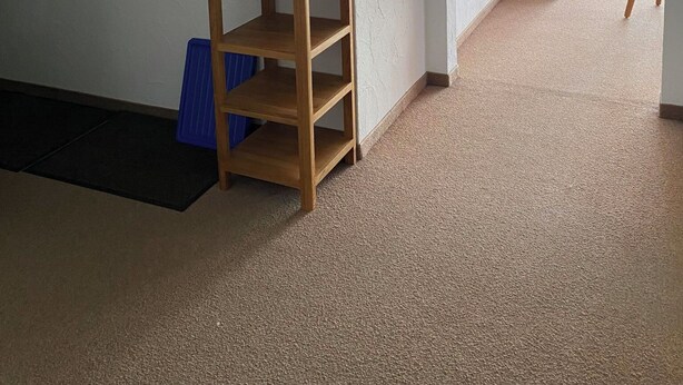 Ein Zimmer mit Holzboden, einem Spiegel an der Wand, einem kleinen Holztisch und einem Stuhl.