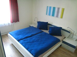 A double bed with blue bedding, a nightstand, a lamp, and a wall-mounted light fixture. - Haus Rhodania Conrad Appartement/Fewo,   5-Bettwohnung (3.5 Zimmerwohnung) by Interhome (Lenzerheide)