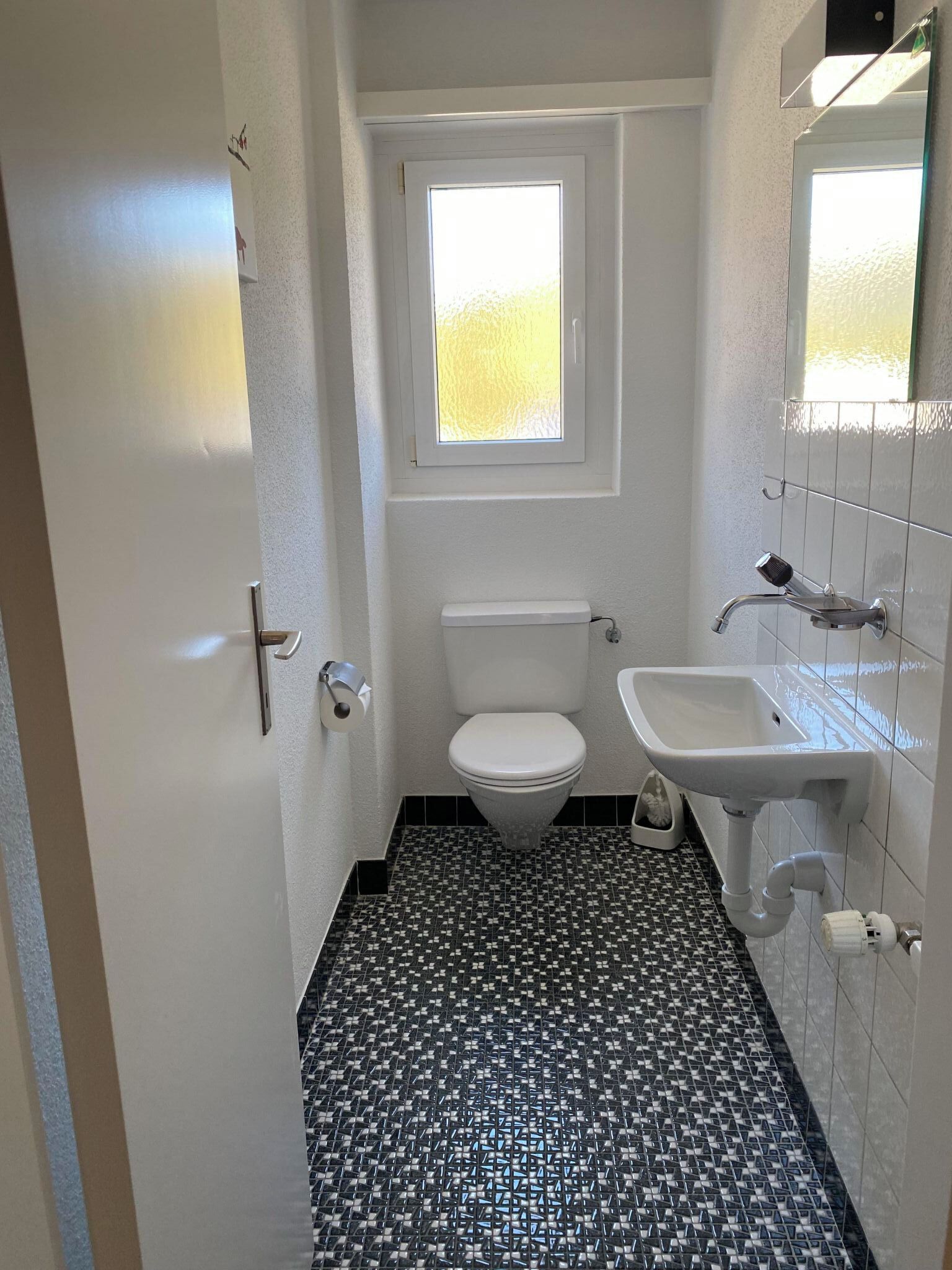 Et lille badeværelse med toilet, håndvask og vindue.