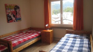 Ein Schlafzimmer mit zwei Einzelbetten, einem Holznachttisch, einem Schreibtisch und einem Fenster mit Vorhängen.