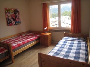 Ein Schlafzimmer mit zwei Einzelbetten, einem Holznachttisch, einem Schreibtisch und einem Fenster mit Vorhängen.
