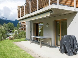 A modern building with a balcony, a covered outdoor grill, and a view of a mountainous landscape.