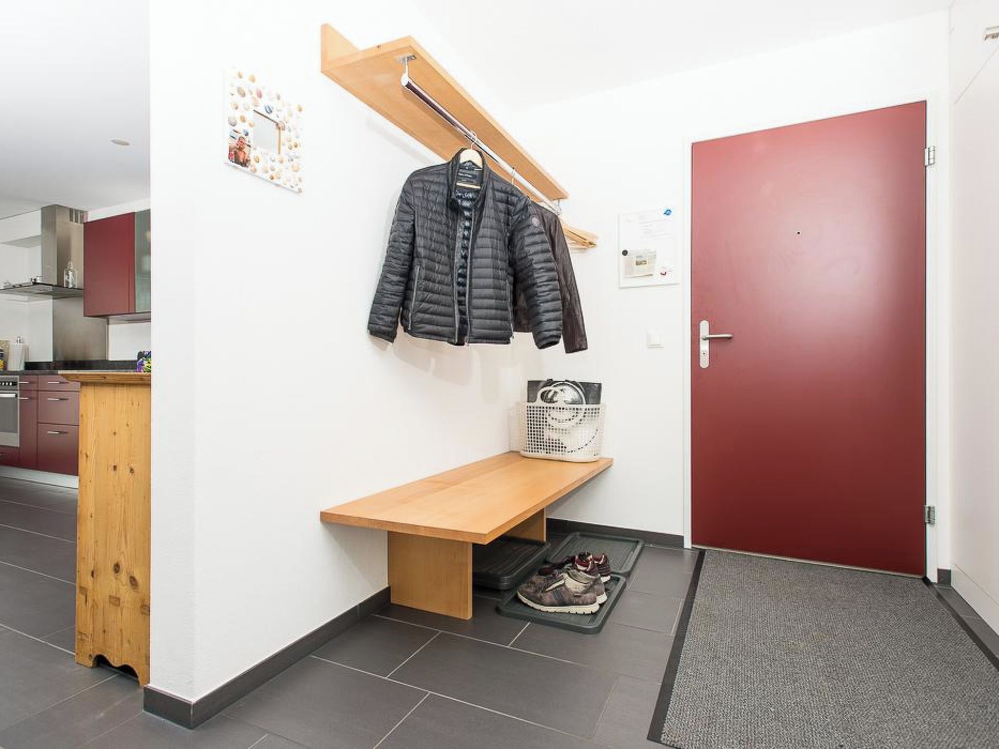 A hallway with a wooden bench, a coat rack with a jacket, a door, and a basket on the floor.