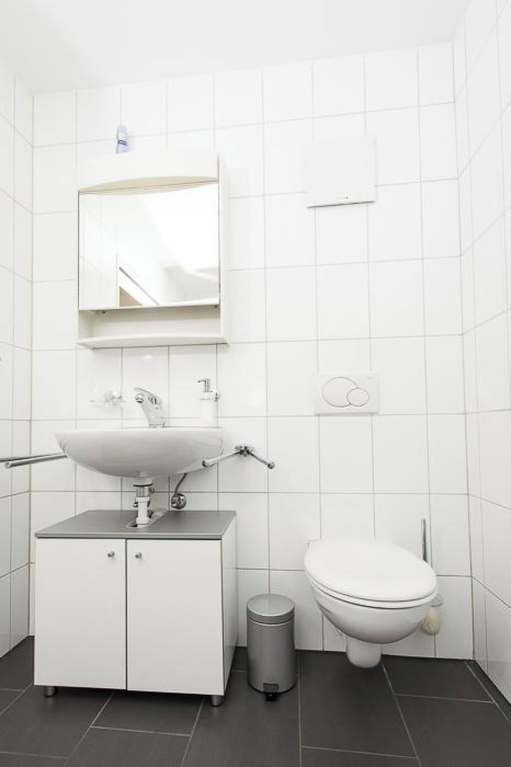 A bathroom with a white sink, mirror, toilet, and trash can.