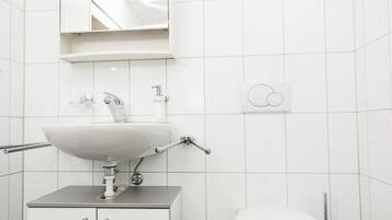 A bathroom with a white sink, mirror, toilet, and trash can.