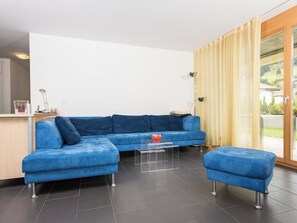 A modern living room with a blue sectional sofa, a glass coffee table, and a matching ottoman.