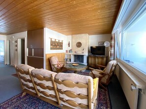 Ett vardagsrum med en soffa, fåtöljer, en öppen spis, en tv och ett fönster.