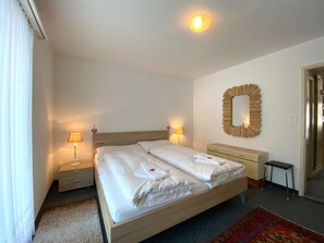 A hotel room with a bed, bedside lamps, a mirror, a dresser, and a carpet. - Haus Montana 2/4 Appartement/Fewo,   4-Bettwohnung by Interhome (Lenzerheide)
