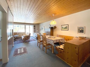 Ett mysigt rum med ett träpanelat tak, ett matbord med stolar, en soffa och ett fönster med utsikt över träd.