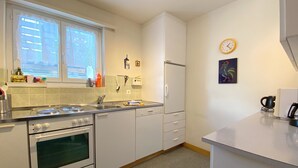 A modern kitchen with white cabinets, a stove, an oven, a sink, and a window with decorative curtains. - Haus Montana 2/4 Appartement/Fewo,   4-Bettwohnung by Interhome (Lenzerheide)